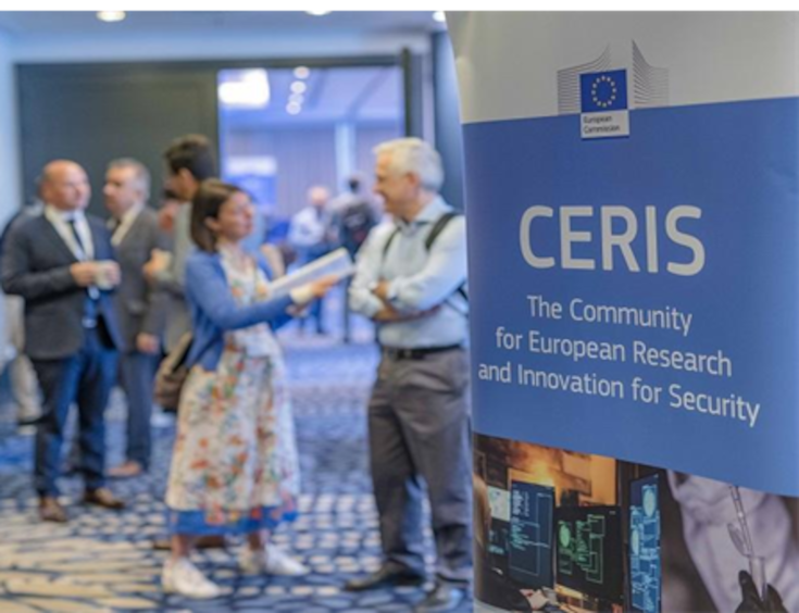 aparece una foto de una sala en la que aparece gente hablando, a la derecha de la foto en un cartel aparece el logo del CERIS