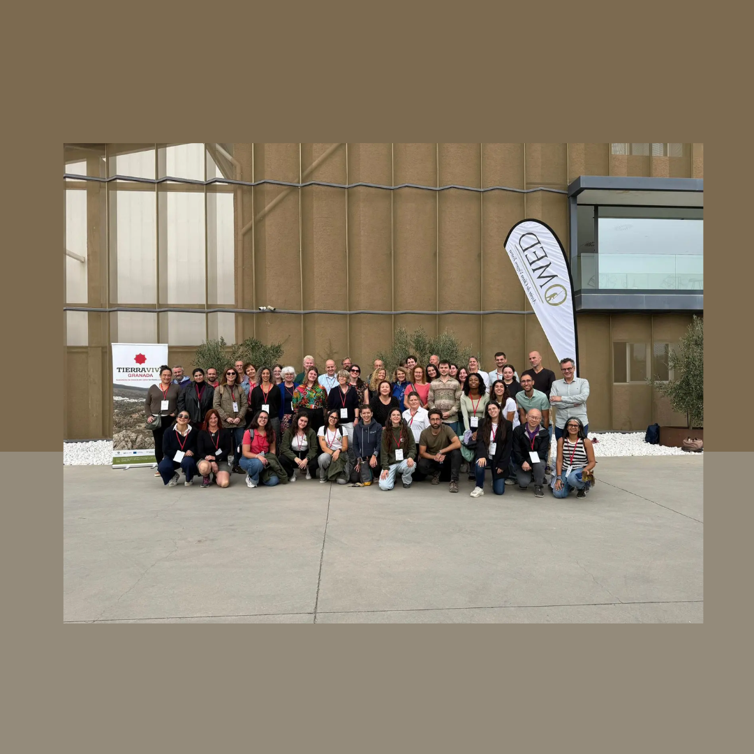 Aparece una imagen un grupo de personas reunidas frente a un edificio moderno durante un evento. Destacan dos pancartas: TierraViva y OWEED, relacionadas con sostenibilidad. Ambiente colaborativo en un contexto profesional o científico.
