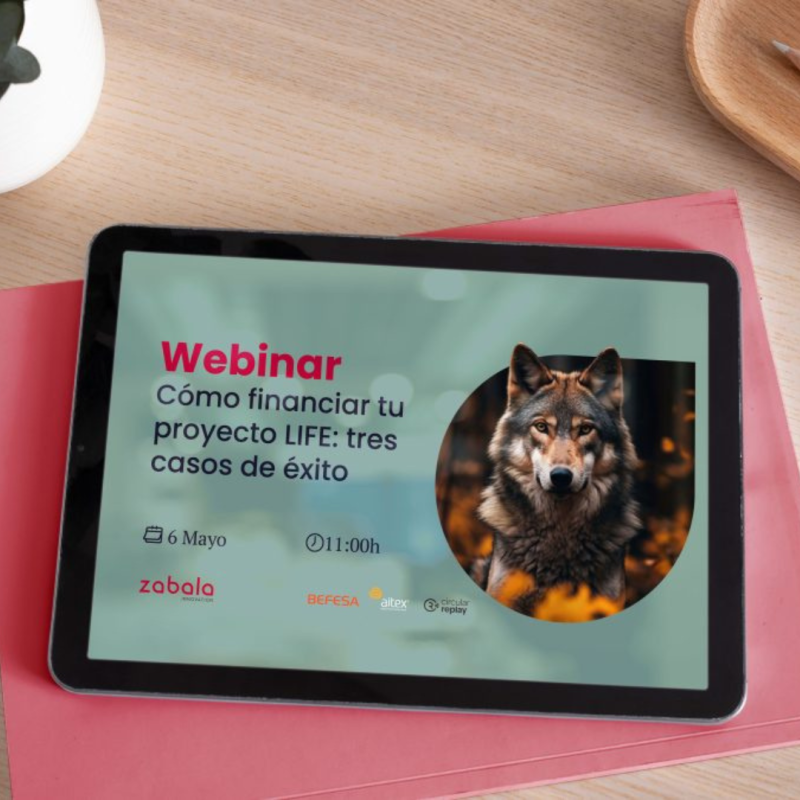 Cartel | Webinario | Cómo financiar tu proyecto LIFE: 3 casos de éxito | 6 mayo aparece una foto de una tableta sobre una mesa de madera. En la tableta se aprecia el cartel de la jornada con los datos básicos de la jornada y una foto de un lobo.